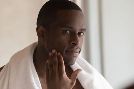 Man with a white towel over his shoulders feeling his hairless face